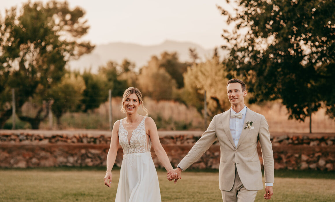 a man and woman holding hands and walking on grass