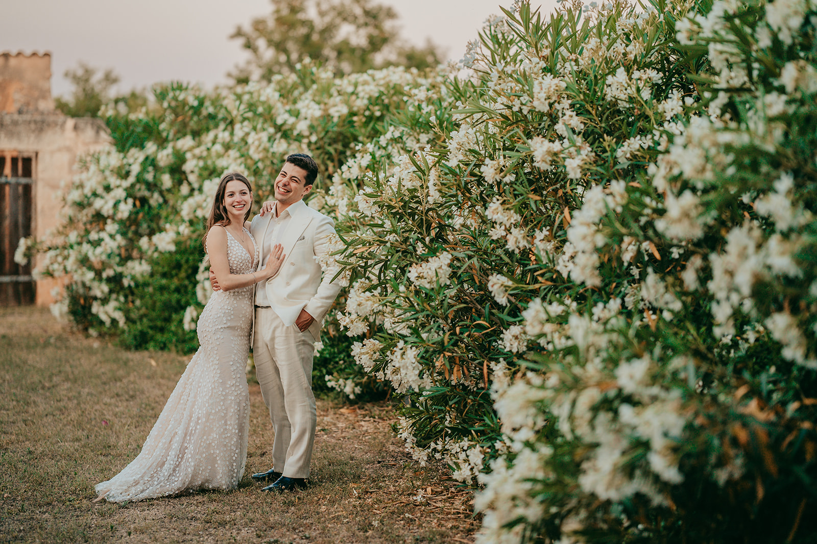 katharina und joshua: finca alaiar Hochzeitspaar gemeinsam lachend vor einer blühenden Olaeanderhecke auf einer Finca