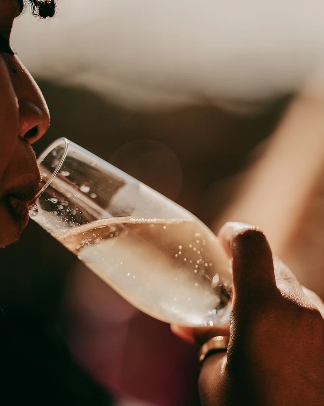 Eine Nahaufnahme einer Person, die Finca Alaiar Sekt in der Hand hält und daran nippt, mit weichem natürlichem Licht und einem unscharfen Hintergrund - die perfekte Inspiration für jeden Hochzeitsfotografen Mallorca.